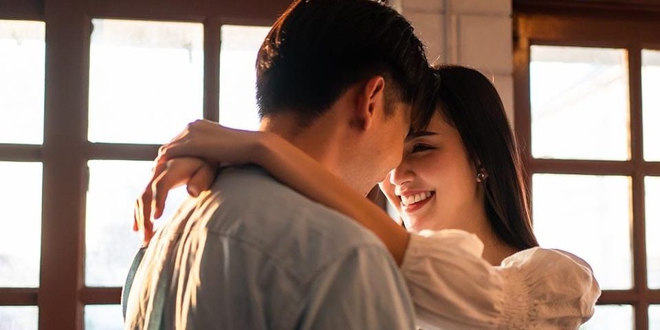 Asian young man and woman hugging each other in living room at home. Attractive romantic new marriage couple male and female spending time celebrate anniversary and valentine's day together in house.