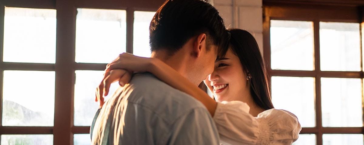 Asian young man and woman hugging each other in living room at home. Attractive romantic new marriage couple male and female spending time celebrate anniversary and valentine's day together in house.